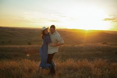 a man and woman hugging in the middle of a field at sunset with mountains in the background