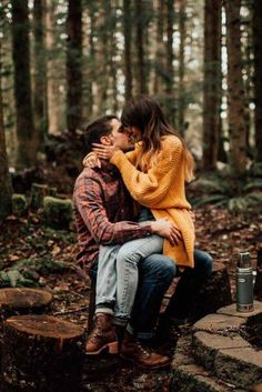 a man and woman sitting on top of a tree stump in the middle of a forest