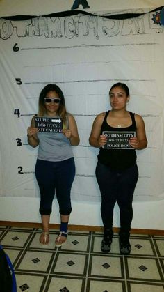 two women holding up signs in front of a white wall with words written on it