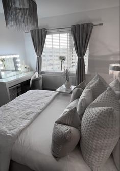 a white bed sitting in a bedroom next to a window with drapes on it