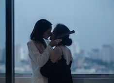 two women standing next to each other in front of a window with cityscape