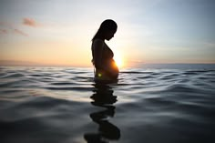 a woman standing in the water at sunset