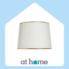 a white lamp shade sitting on top of a light blue background with the at home logo below it