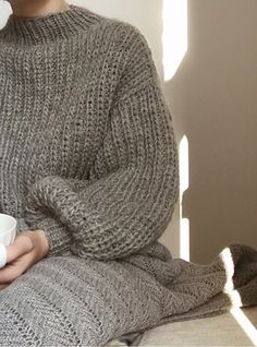 a woman is holding a cup and wearing a sweater