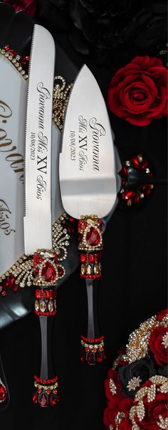 two knifes with red and gold decorations on them next to each other in front of roses