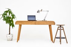 a wooden desk with a laptop on it next to a stool and potted plant