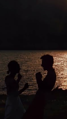 two people standing next to each other in front of the water at sunset or sunrise