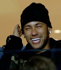 a smiling man wearing a black beanie and earring in front of a crowd