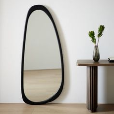 a mirror sitting on top of a wooden table next to a vase with a plant in it