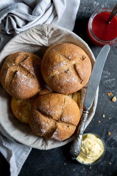 four rolls in a bowl with butter on the side and a knife next to it