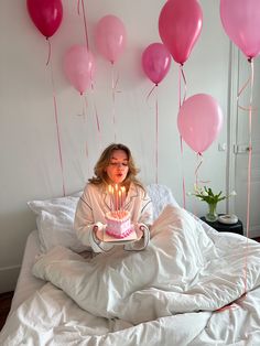 a woman sitting on top of a bed holding a cake with lit candles in front of her