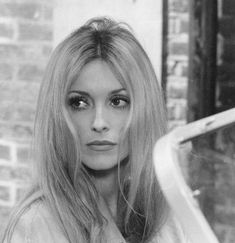 a black and white photo of a woman with long hair in front of a brick wall