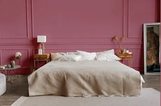 a bedroom with pink walls and white bedding, two nightstands and a chair