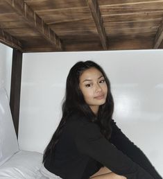 a young woman sitting on top of a bed under a wooden roof over her head