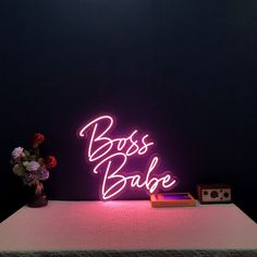 a pink neon sign that says boss babe on top of a white table with flowers