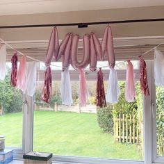 some pink and white balloons hanging from the ceiling in front of a window with grass