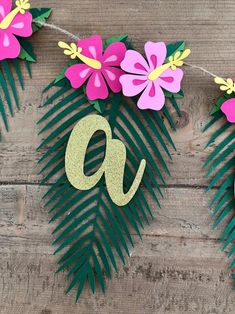 some paper flowers and leaves are hanging on a string with the letter q in gold