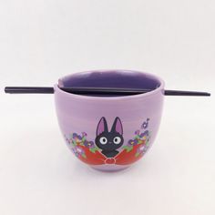 a purple cup with a black cat on it and two chopsticks sticking out of it