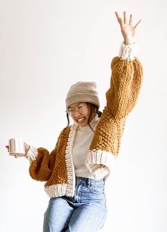 a woman is jumping in the air with her hands up and holding a coffee cup