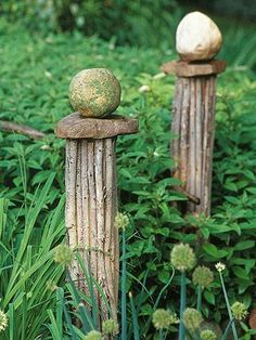 two wooden posts with balls on them are in the middle of some green plants and grass