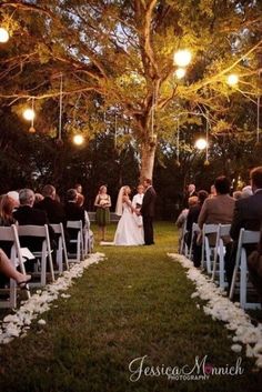 a bride and groom standing under a tree at their wedding ceremony in the evening with lights hanging from the trees