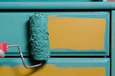 a person is painting a dresser with green and yellow paint on the drawers, holding a roller