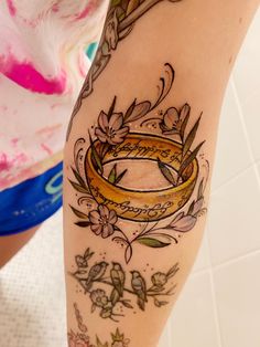 a woman's leg with a tattoo on it that has a gold ring in the middle