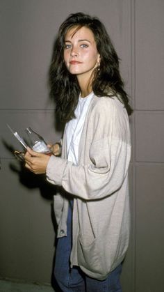 a woman standing in front of a wall holding a book and looking at the camera