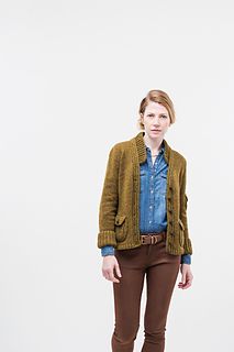 a woman standing in front of a white wall wearing brown pants and a blue shirt