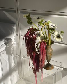 two vases with flowers in them sitting on a glass shelf next to a mirror