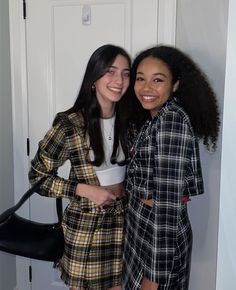 two young women standing next to each other in front of a white door and smiling at the camera