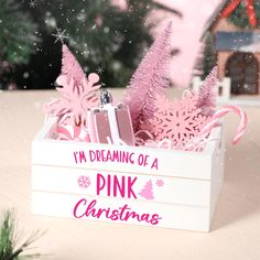 pink christmas decorations in a white box on a table with snowflakes and trees