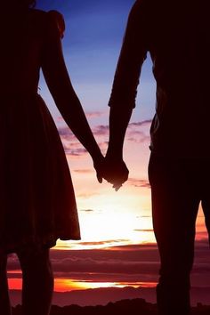 two people holding hands with the sun setting in the background