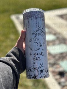 a person holding up a coffee cup with writing on the side and flowers painted on it