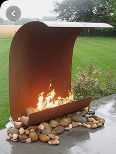 a fire pit sitting on top of a patio next to a lush green field with lots of trees