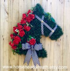 a wreath made out of fake red roses on a wooden fence with a ribbon tied around it