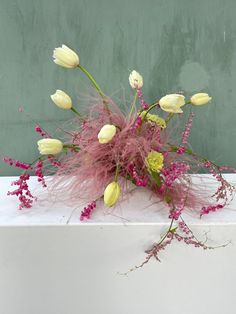 a bouquet of flowers sitting on top of a white table next to a green wall