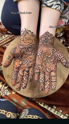 two hands with henna tattoos on them sitting on top of a round plate in front of