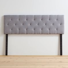 an upholstered headboard with black metal legs on a wooden floor in front of a white wall