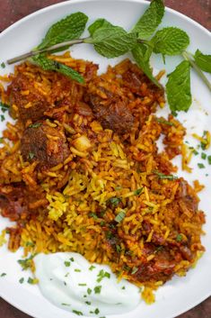 a white plate topped with rice and meat next to minty garnishes