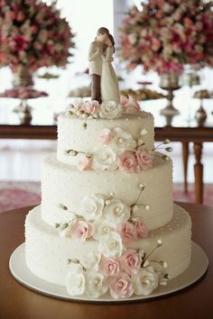 a white wedding cake with pink flowers and a bride and groom figurine on top