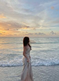 a woman in a long dress standing on the beach