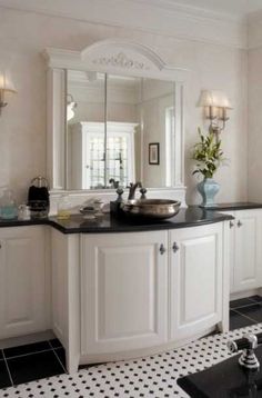 a bathroom with black and white tile flooring and walls, along with a large mirror on the wall