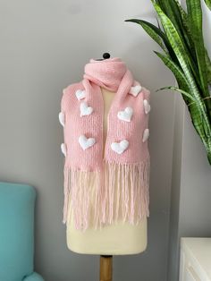 a pink scarf with white hearts on it sitting on a mannequin next to a potted plant