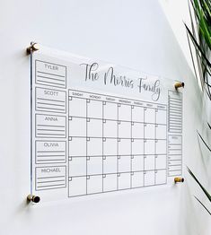 a wall mounted calendar on the side of a white wall next to a potted plant