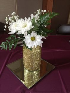 a vase filled with white flowers sitting on top of a purple tablecloth covered table