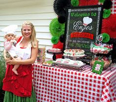 a woman holding a baby standing in front of a table with food and decorations on it