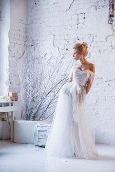 a woman in a white dress is standing near a brick wall and looking off to the side