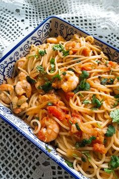 a blue and white bowl filled with pasta, shrimp and parsley garnished with cilantro