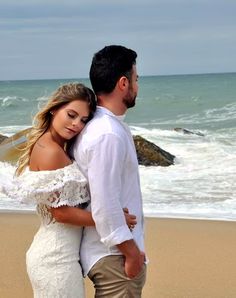 a man and woman are standing on the beach looking at the ocean while holding each other